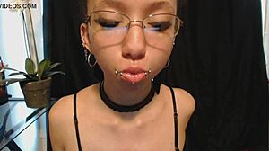 The young goth girl puts on nude lipstick and drools all over it, her tongue and saliva making a mess.