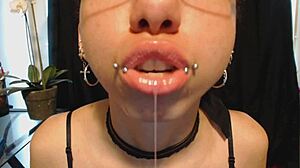 The young goth girl puts on nude lipstick and drools all over it, her tongue and saliva making a mess.