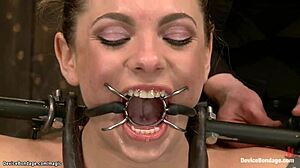 Latex-clad sub gags in bondage as blonde domme chokes her deep in metal device